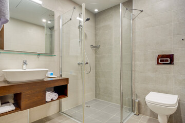 A spacious modern bathroom with a clean design, featuring a glass shower, a wooden vanity unit, and tiled walls. The elegant fixture placement creates a comfortable and functional space.