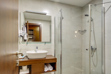 A spacious modern bathroom with a clean design, featuring a glass shower, a wooden vanity unit, and tiled walls. The elegant fixture placement creates a comfortable and functional space.