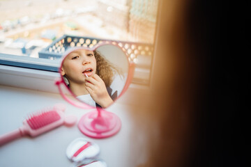Young girl applying lip gloss while looking in a heart-shaped mirror