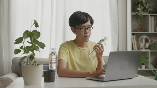Asian man multitasking at home working on laptop while lifting dumbbells for exercise.4k