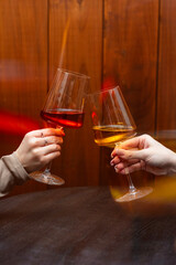Close-up of two woman hands clinking elegant wine glasses filled with red and white wine in warm candlelit atmosphere.