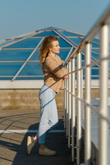 Young woman gazing at the sea while leaning on a railing by the waterfront in bright sunlight