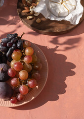 Plate with ripe figs fruit, bunches of grapes, brie cheese and nuts on the mediterranean pink...