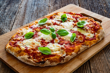 Pinsa Margherita with tomato sauce, basil leaves and mozzarella cheese on wooden background