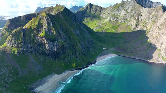 Captivating landscapes showcase the stunning Ryten Kvalvika Trail in Lofoten, Norway, highlighting lush mountains and turquoise waters along the pristine coastline during a sunny day.