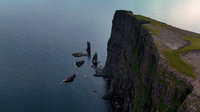Majestic Risin og Kellingin sea stacks stand tall against the tranquil waters, showcasing the unique beauty of the Faroe Islands. Explore the breathtaking landscape where nature meets folklore.