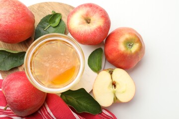Fresh cider in glass, apples and green leaves on white table, flat lay