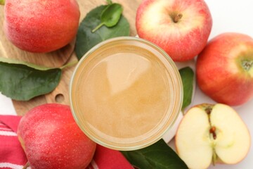 Fresh cider in glass, apples and green leaves on white table, flat lay