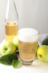 Fresh cider in glass, bottle and apples on white wooden table, closeup