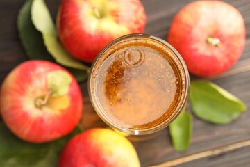 Delicious cider in glass, apples and green leaves on wooden table, flat lay