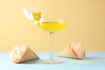 Tasty cocktail with cotton candy and waffle cones on color background