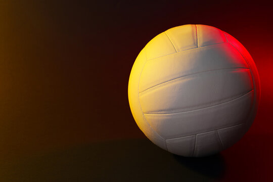 White volleyball ball on dark background in color lights. Space for text