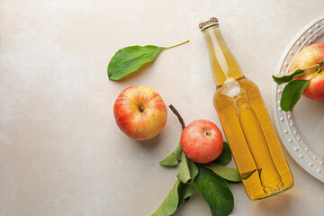Delicious cider in glass bottle and apples with green leaves on beige table, flat lay. Space for text