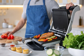 Man cooking vegetables and meat on electric grill in kitchen, closeup