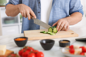 Cooking process. Man cutting cucumber at table indoors, closeup