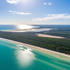 High-angle view of a coastal landscape with turquoise water, white sand beaches, and lush green forests. Sunlight highlights the water