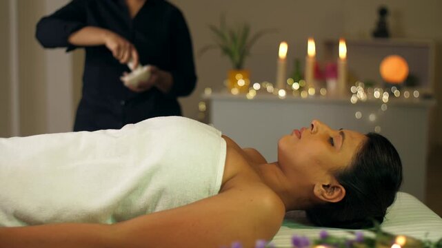 A professional massage therapist prepares a spa massage for a young Indian girl at a spa salon  relaxing environment. A girl enjoys a massage at the spa - luxury professional massage  relaxing mass...