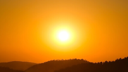 Strong sunlight shining in the orange golden yellow sky with mountain. Heat wave in the summer.