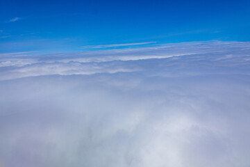 High altitude aerial photograph of fluffy white clouds and blue sky taken from an airplane window