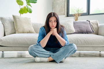 Fototapeta premium Sad upset young woman with sitting on floor near sofa at home