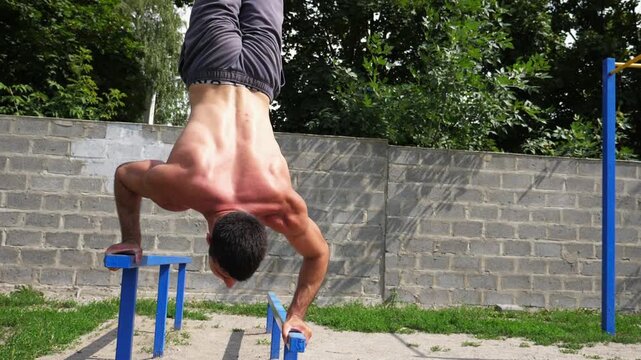 Sportsman performing dynamic handstand push-up training on parallel bars, showcasing strength and balance in a progressive workout sequence with vibrant greenery in the background