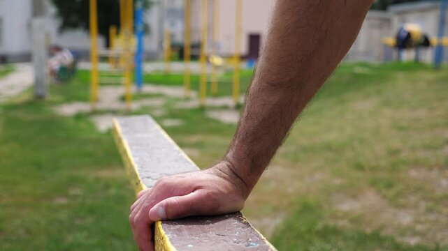 Sportsman performing intense workout on parallel bars, showcasing strength and focus as hands grip the weathered surface highlighting determination and physical training progression in outdoor setting