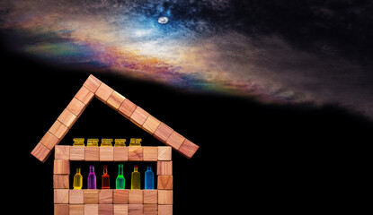 Wooden cubes arranged to form a simplistic house with various miniature bottles of alcohol without labels and gold bars in the attic against black bacground
