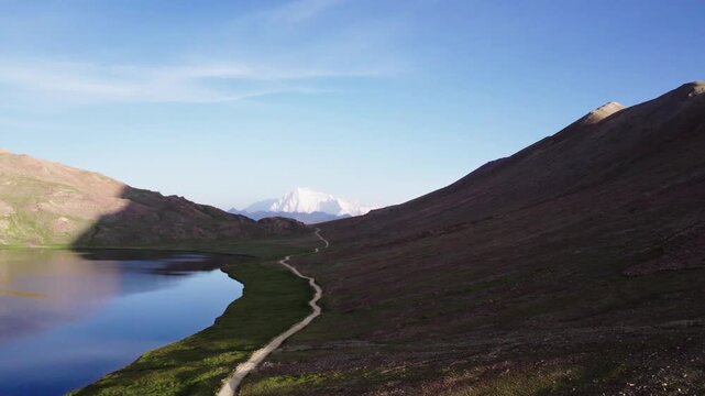 Dirt road along Sheosar Lake leads toward distant Nanga Parbat in Deosai&rsquo;s high-altitude meadows