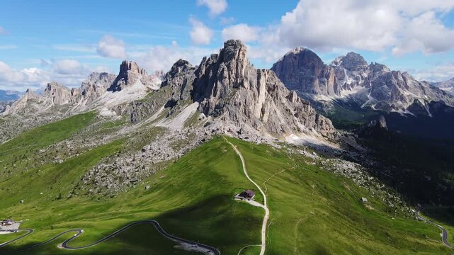 Drone backward, Ra Gusela peak above green Passo Giau slopes, Italy Dolomites