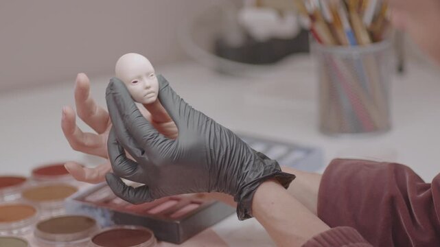 Artist fitting eyes into doll head focusing on fine details and precision needed to create realistic facial features, demonstrating expert craftsmanship in doll making at workshop