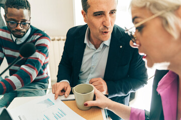 Diverse business professionals collaborating and analyzing financial charts. Colleagues brainstorming over data, concept of teamwork, strategy and market research during a meeting .