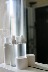 Care products, cosmetics and comb on the shelf in white bathroom. Cleanser, lotion, cream and comb near mirror. White bathroom. Women care products. Yellow comb. 