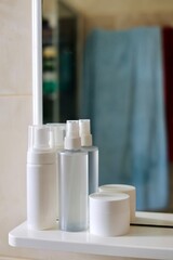 Care products, cosmetics and comb on the shelf in white bathroom. Cleanser, lotion, cream and comb near mirror. White bathroom. Women care products. Yellow comb. 