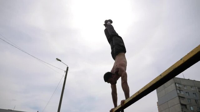 Sportsman performing dynamic workout on parallel bars, showcasing strength and control through progressive movements in an outdoor training environment with vibrant grass and exercise equipment