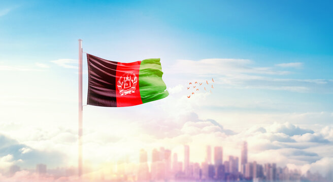Afghanistan flag wavering in beautiful clouds with building skyline. The flag with drone shot in beautiful sky. Afghanistan national flag for independence day.