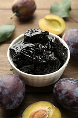 Dried prunes, fresh plums and green leaves on wooden table, closeup