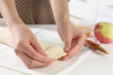 Woman making delicious apple strudel at white wooden table in kitchen, closeup