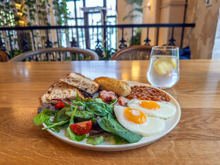 Hearty English Breakfast Spread: A Classic Morning Meal Featuring Fried Eggs, Bacon, Baked Beans, Toast, and a Fresh Salad in a Cozy Cafe Setting