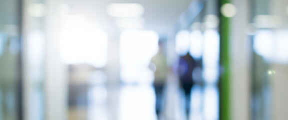 Blurred figures walk in a bright modern building hallway with glass walls, evoking motion and the lively atmosphere of contemporary architecture in an urban space.