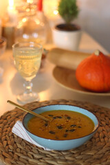 Plate of pumpkin soup, pumpkins, glass of wine, nuts and lit candles on the table. Selective focus.