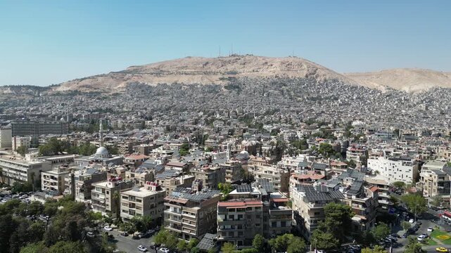 An aerial view captures the new Syrian national flag hoisted on a towering pole in central Damascus, with Mount Qasioun, one of the capital&rsquo;s most prominent landmarks rising in the background.