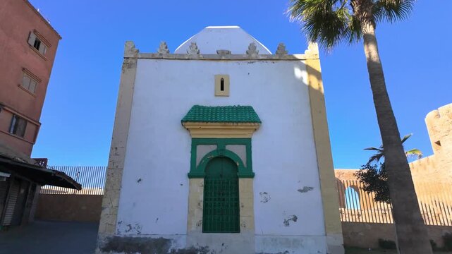 Front view of a traditional white Moroccan building with a green door in Safi, Morocco, framed by palm trees and blue sky. A striking example of local architecture and cultural charm in a coastal city