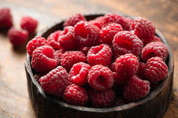 Raspberries in wooden bowl on old wooden table background, closeup view. Summer berry harvest
