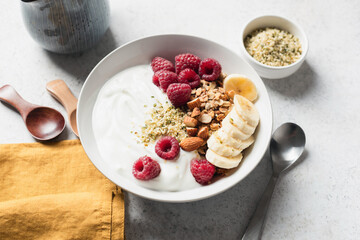 Yogurt bowl with raspberroes, banana and muesli granola on grey table background. Concept of clean eating, dieting, healthy fitness meal