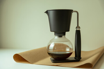 Modern glass coffee pot with black handle brewing fresh hot coffee on minimal light background for contemporary kitchen aesthetics