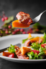 Delicious salad with bacon and pumpkin on a white plate