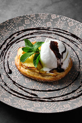 Delicious apple tart with ice cream and chocolate syrup on a decorative plate.