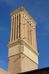 Fototapeta premium Traditional windcatcher tower in Yazd, Iran, ancient Persian architecture for natural cooling, historic adobe structure against blue sky.