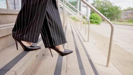 Woman navigates stairs and walkway in high heels while dressed in stylish pantsuit near modern building in urban setting