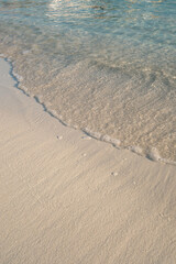 Minimal, people-free close-up of a gentle wave with foam over smooth sand and clear shallow water on the Ionian coast in Ksamil, Albania—versatile for travel, wellness and resort branding, with copy s
